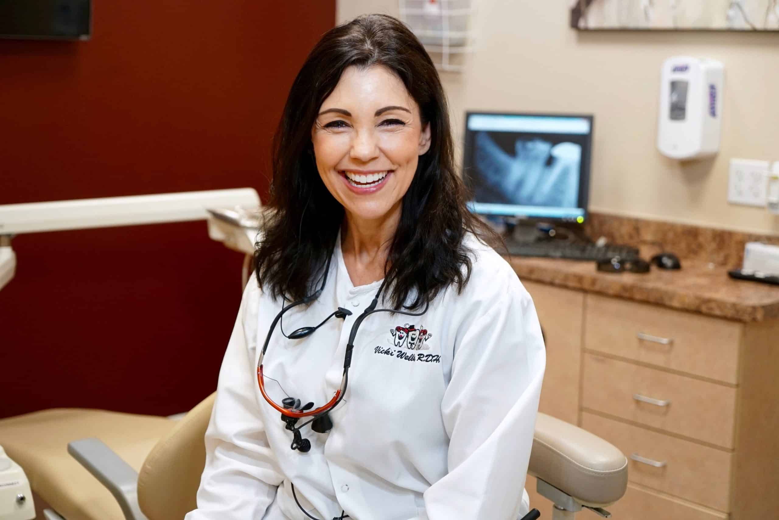 Victoria, a BDG dental hygienist, smiling from her chair in a dentist office room with a dental x-ray in view on a screen behind her