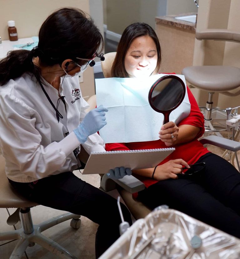 dentist with patient, explaining a dental procedure as the patient reviews her smile with a round mirror