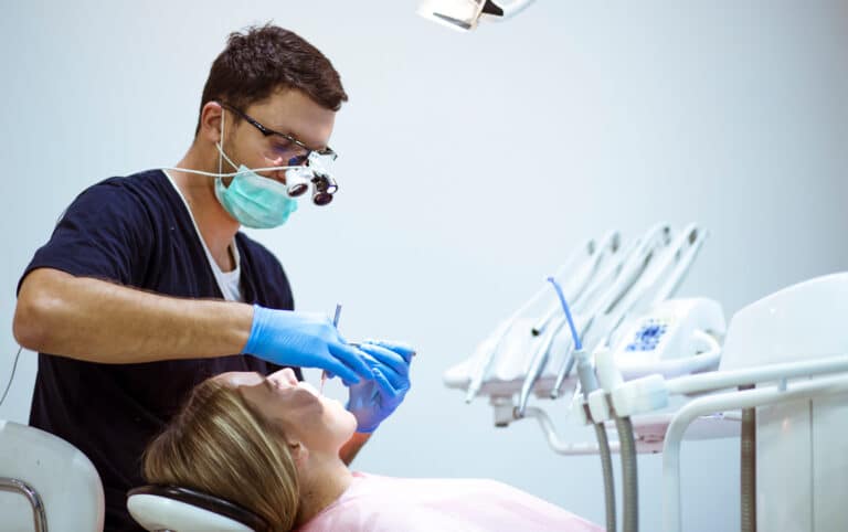 Woman getting checked up during an emergency dental visit, the dentist wearing light scopes and examining her mouth