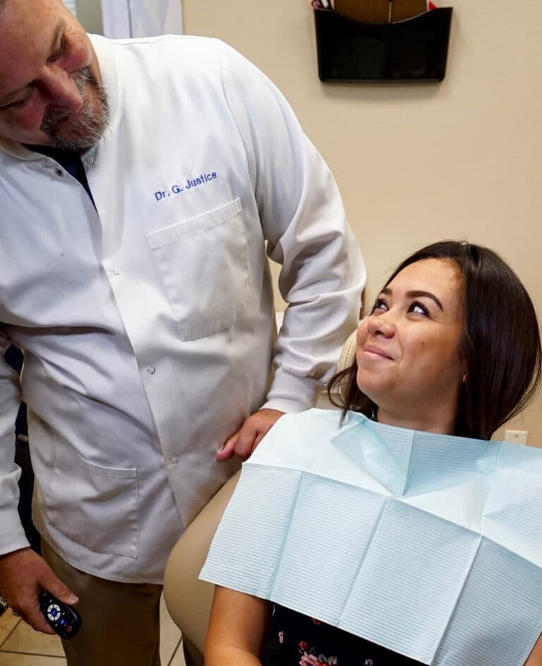 happy patient smiles up at her overlooking dentist, leaning over her chair