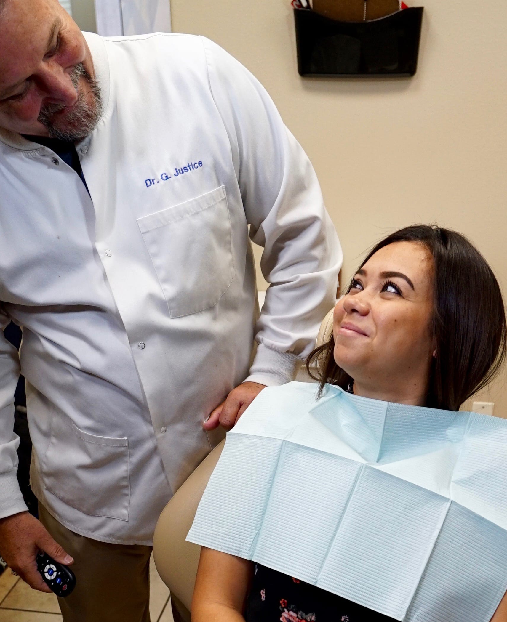 happy patient smiles up at her overlooking dentist, leaning over her chair