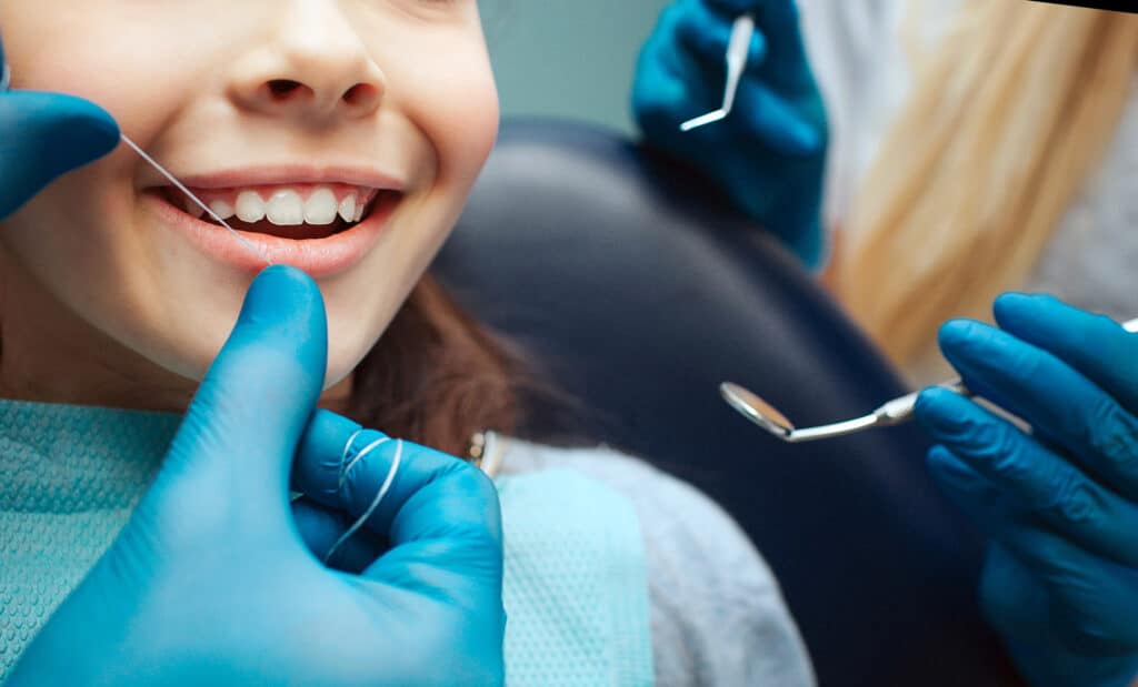 Child at dentist - Cut view hands in latex gloves to floss child front teeth. Woman hold dental tools beside