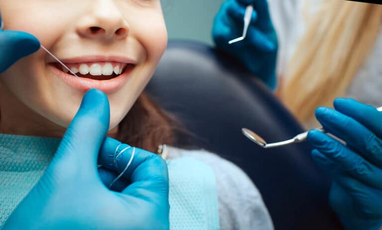 Child at dentist - Cut view hands in latex gloves to floss child front teeth. Woman hold dental tools beside