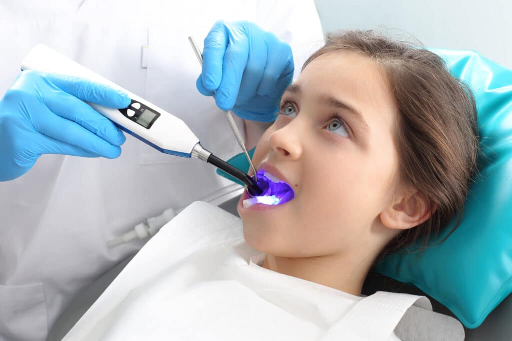 Child in the dental chair with light cure for dental sealants or after surgical procedure